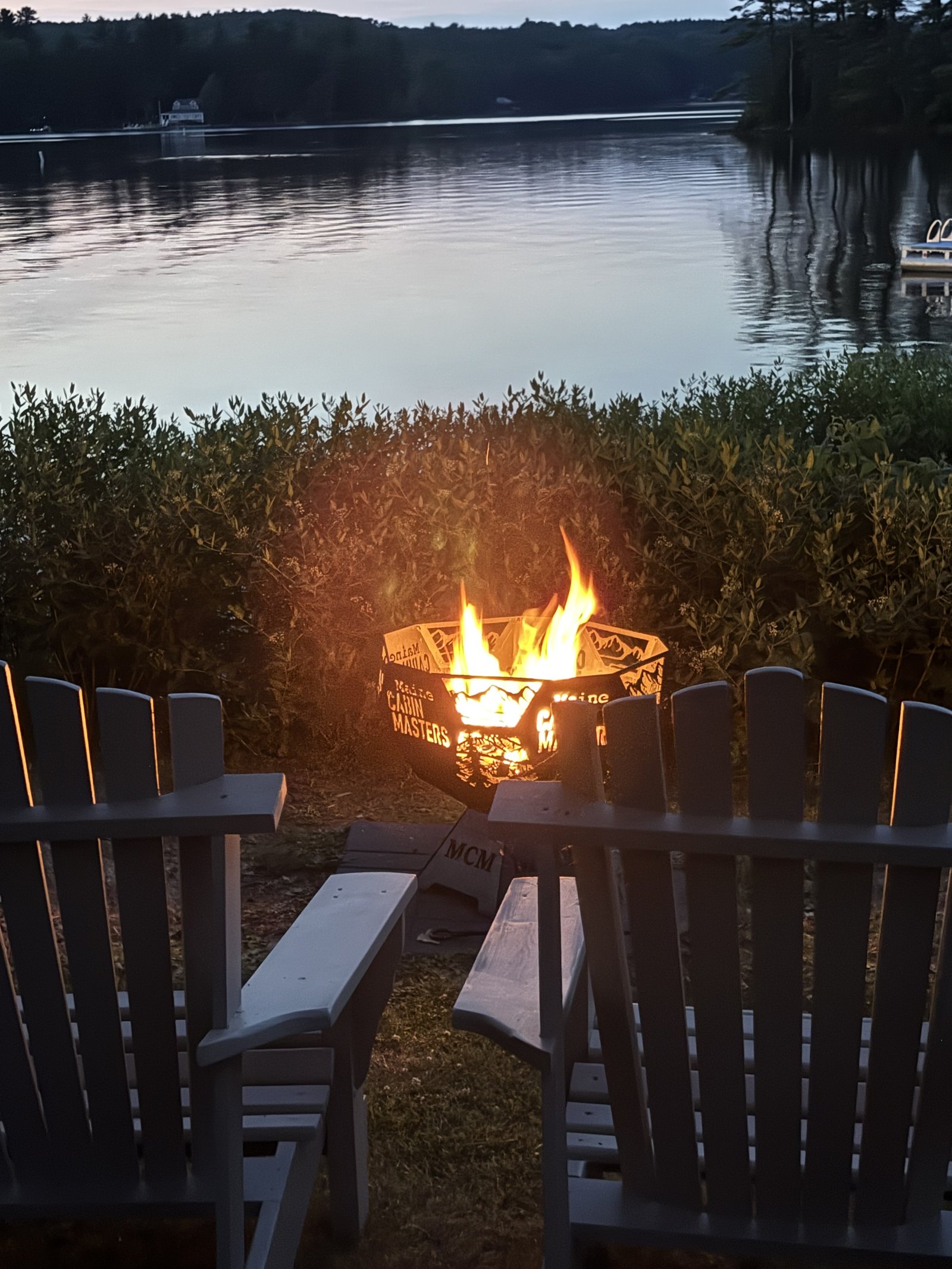 Evening fire pit overlooking Maranacook Lake, with Adirondack chairs and the dock visible in the distance